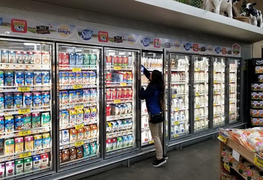 HAP merchandiser stocking a dairy cooler wall topped with Silk, Horizon Organic, So Delicious, and International Delight header banners in a grocery store