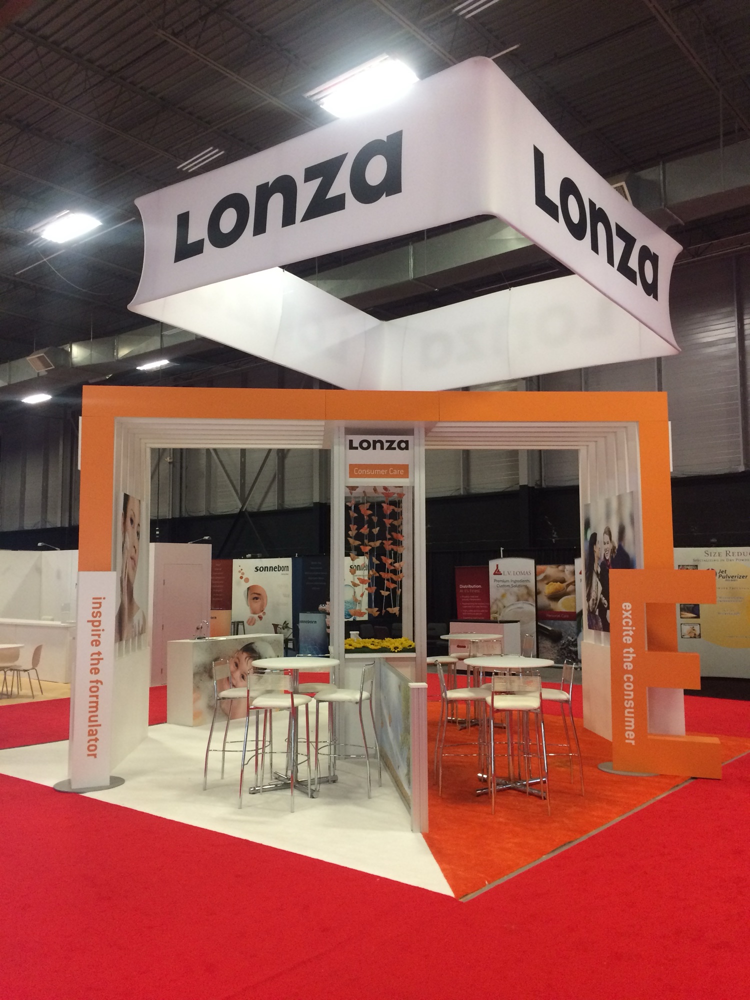 Lonza Consumer Care booth with orange portal structure, square hanging banner, and giant letter E