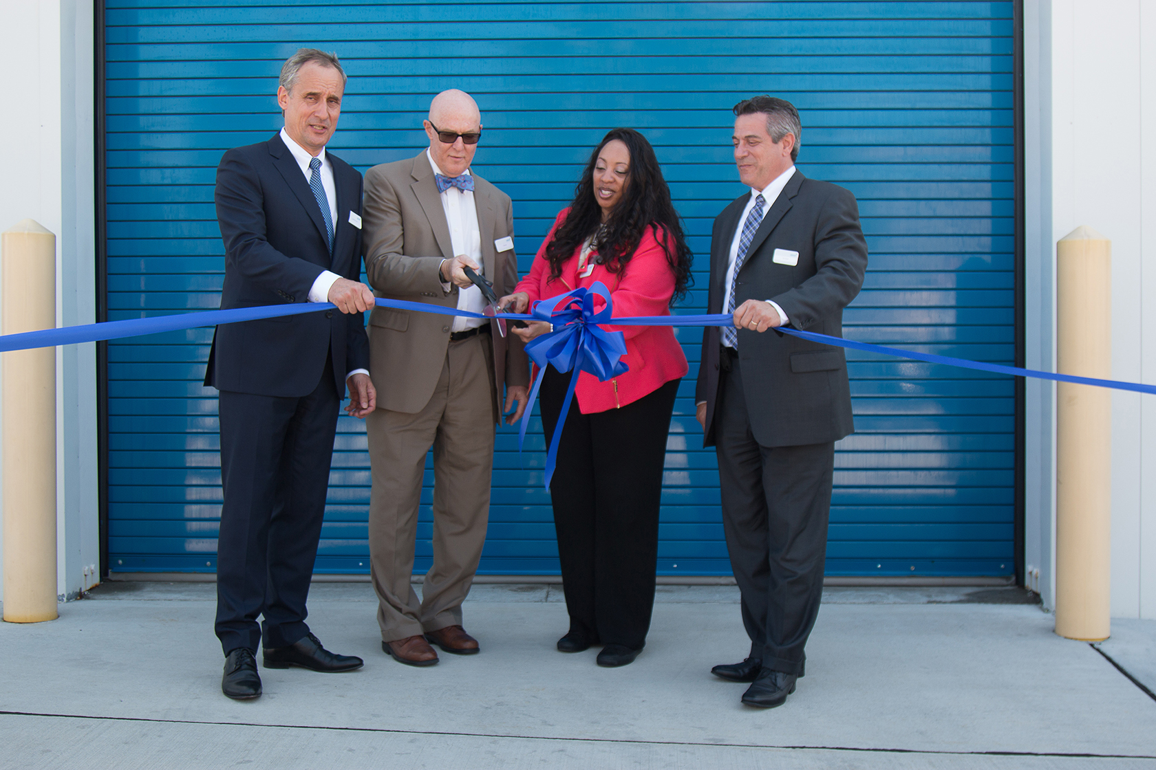 Ribbon-cutting ceremony with executives cutting a blue ribbon at a facility entrance