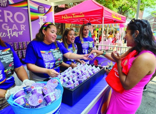 Staff in Oikos T-shirts at a purple event tent handing yogurt samples to a passerby